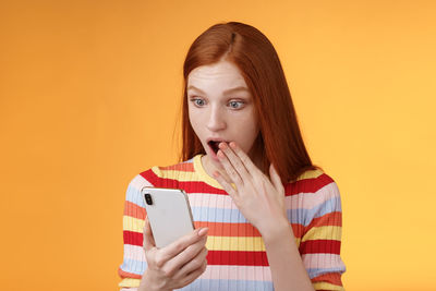 Portrait of young woman using phone against orange background