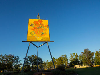 Low angle view of yellow sign against blue sky