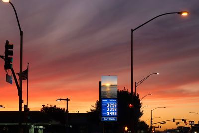 Illuminated street lights in city against orange sky