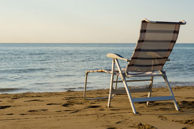 Deck chair on shore at beach against clear sky