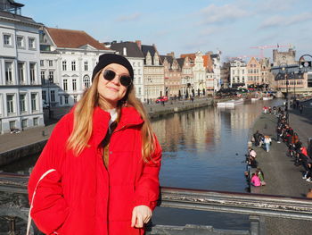 Portrait of beautiful woman standing by canal in city