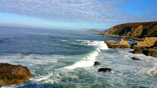 Scenic view of sea  waves and cliffs against sky