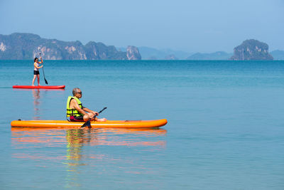 Asian senior father playing standing up paddle board daughter at blue sea on summer vacation