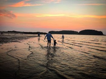 Silhouette people standing on beach against sky during sunset