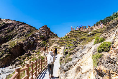 Rear view of man walking on mountain against clear blue sky