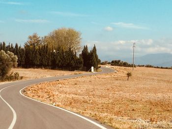 Road amidst trees on field against sky