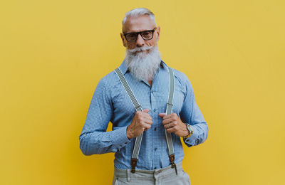 Midsection of man with arms raised standing against yellow background