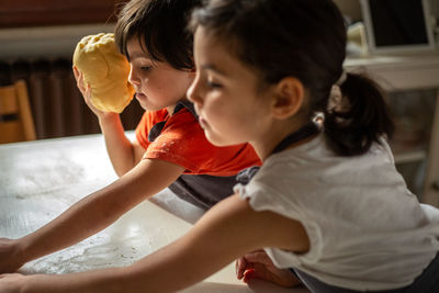 Side view of two girls wearing t-shirts preparing dough at home