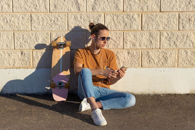 Young hipster man on a bun hairstyle sitting on the floor with a skate board  listening to music