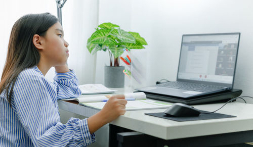 Side view of woman using phone while sitting on table