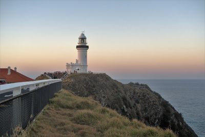 Lighthouse amidst buildings and sea against sky during sunset