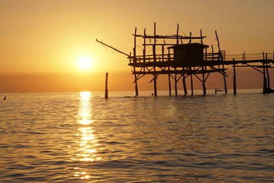 Silhouette built structure in sea against sunset sky