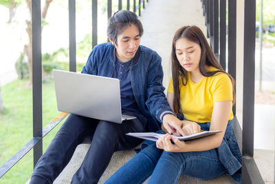 In the university campus, two asian couples sit on the stairwell with their thumbs up, working