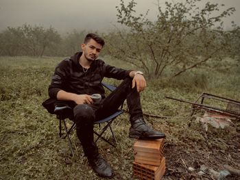 Full length of man sitting against against trees outdoors