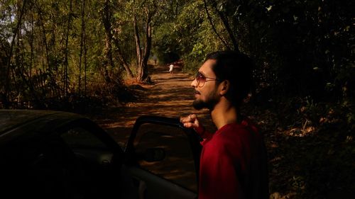 Profile view of man standing with car in forest