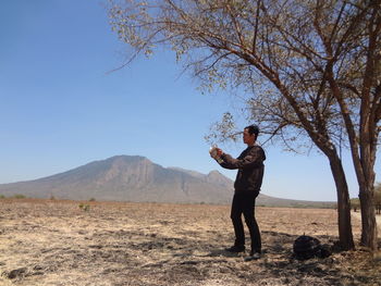 Side view of man standing by tree on mountain