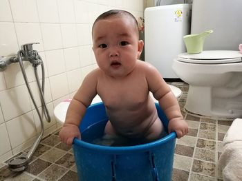 Portrait of cute baby boy standing in bucket at bathroom