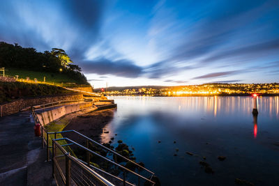 View of illuminated city by river against cloudy sky