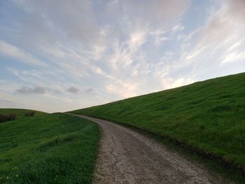 Scenic view of road amidst field against sky