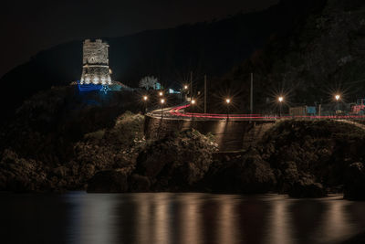 Illuminated bridge over river against sky at night