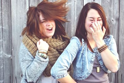 Happy female friends against wooden fence