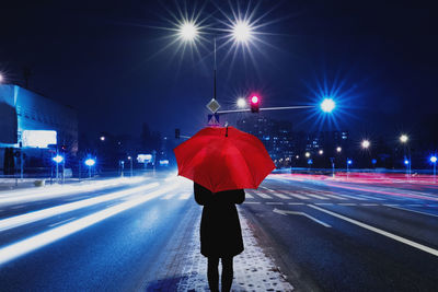 Rear view of woman with umbrella on street at night