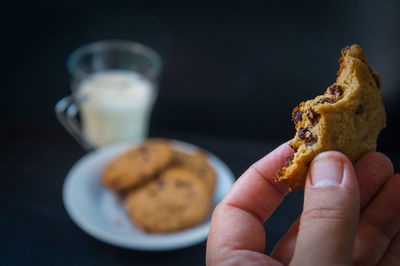 Close-up of hand holding a chocolate cookie against black background