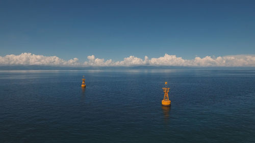 Orange buoy in the blue sea on a background of blue sky, clouds, island. 
