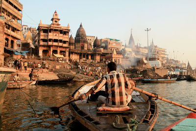 Rear view of man sailing boat on ganges river by temples
