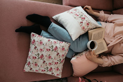 High angle view of woman reading book sitting on sofa at home