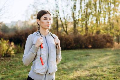 Girl with skipping rope on her shoulders looking thoughtfully, autumn sunny day.