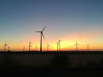 Silhouette wind turbines on field against sky during sunset