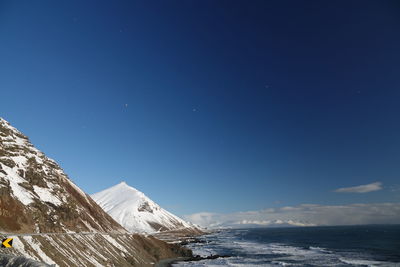 Scenic view of sea by snowcapped mountain against blue sky