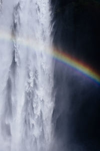 Breathtaking scenery of rainbow shining over rapid powerful skogafoss waterfall flowing through rocky cliff in iceland