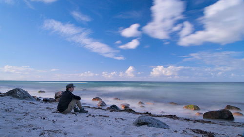 Side view of man sitting on baltic sea shore against sky