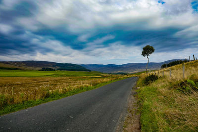 Empty road amidst field against sky