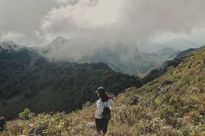 Woman standing on mountain against cloudy sky