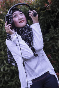 Woman listening music while standing against plants