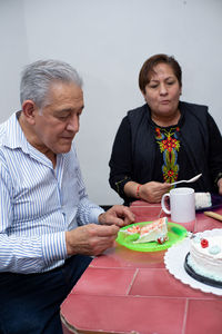 An older man with his friends celebrating his birthday, eating cake at an indoor party.