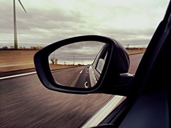 Car reflecting in side view mirror against sky