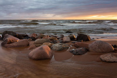 Rocks on beach against sky during sunset