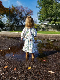 Rear view of girl standing by tree against sky