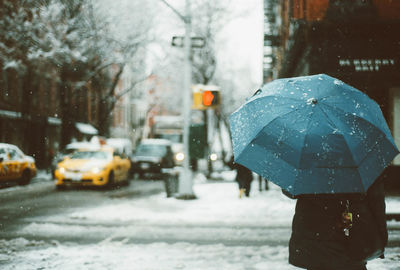 Rear view of person with umbrella standing on road during winter