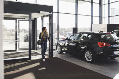 Full length of young woman entering car showroom