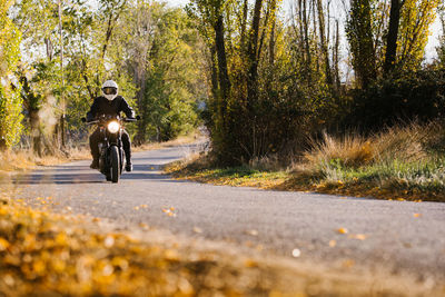 Man in leather jacket and helmet riding bike on asphalt road in sunny autumn day in countryside