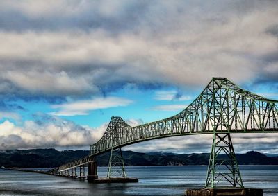 View of suspension bridge over river against cloudy sky