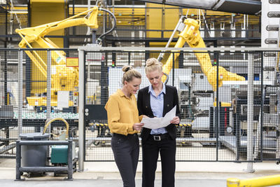 Two women discussing plan in factory shop floor with industrial robot