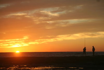 Silhouette men standing at beach against sky during sunset