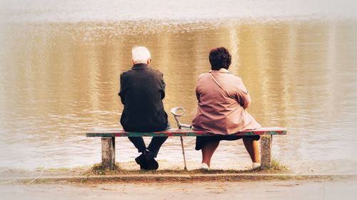 Rear view of friends sitting on shore at lake