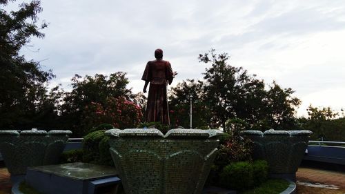 Rear view of man standing by statue against sky